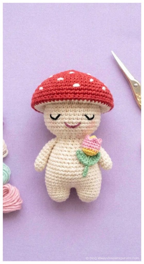 Red mushroom doll amigurumi holding a tiny flower, cute handmade crochet gift idea