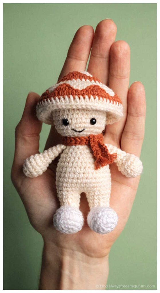 Small mushroom doll amigurumi with scarf in hand, adorable handmade crochet toy idea