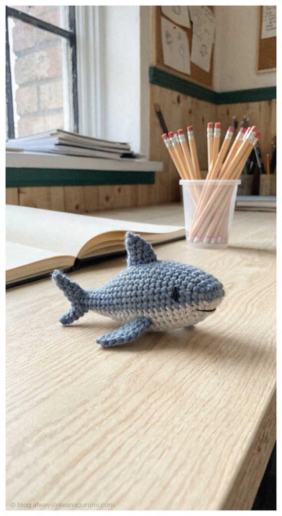 small gray crochet shark amigurumi on a wooden desk cute handmade ocean animal toy crochet project