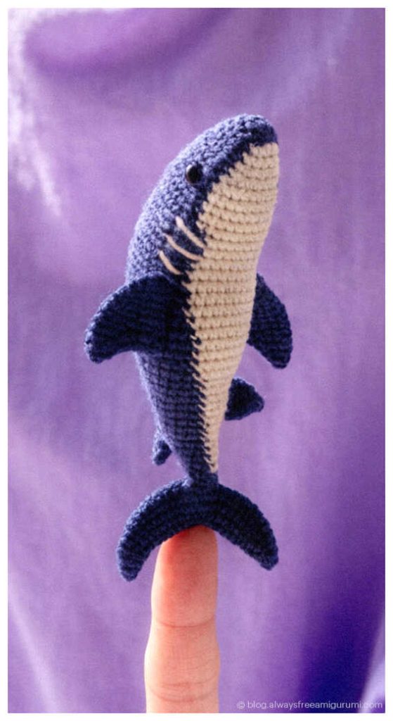 tiny crochet shark amigurumi balanced on a fingertip small handmade ocean animal toy close up