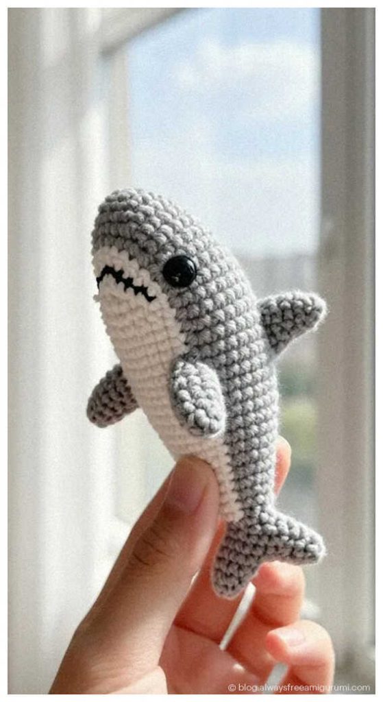 small gray crochet shark amigurumi held between fingers cute handmade ocean animal toy