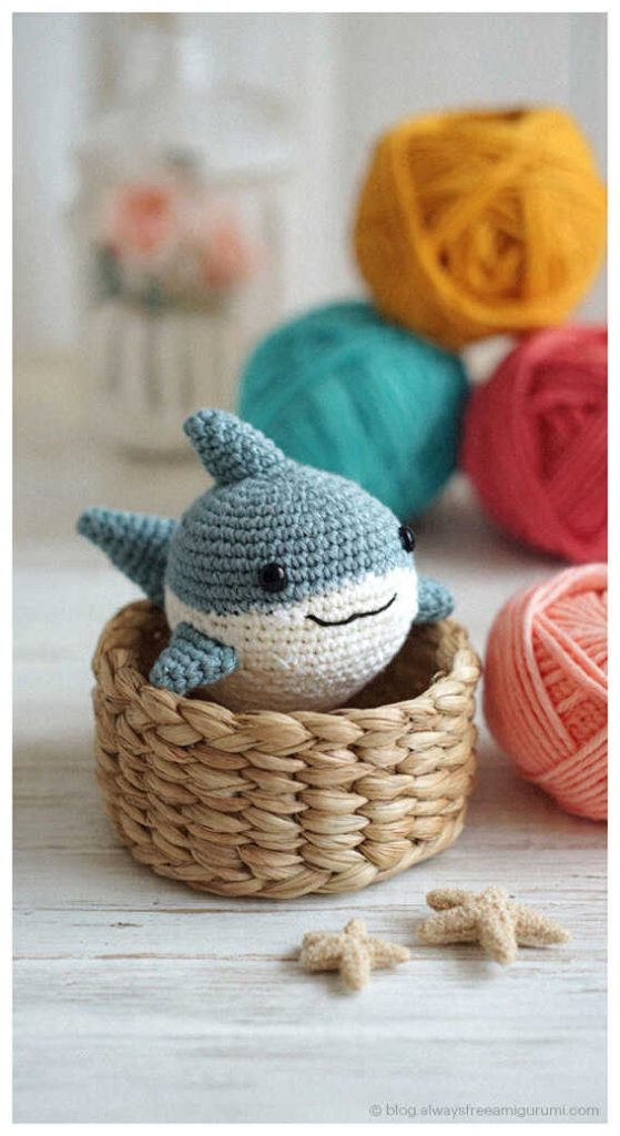 mini crochet shark amigurumi sitting in a small basket with colorful yarn cute handmade ocean animal toy