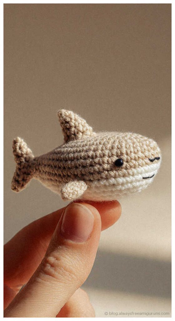 tiny beige crochet shark amigurumi held between fingers small handmade ocean animal toy close up