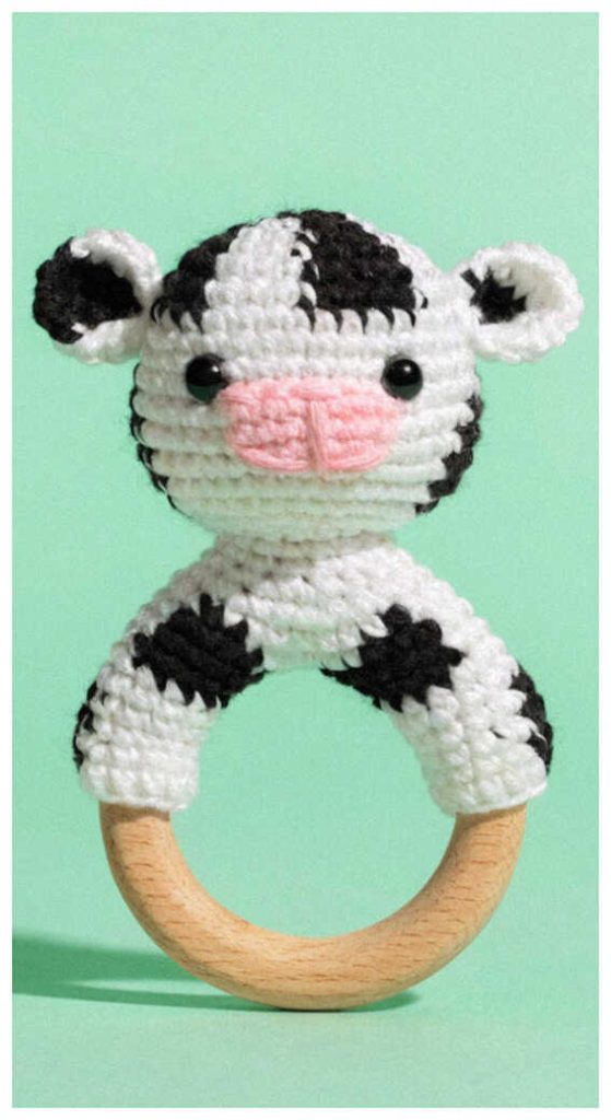 crochet cow baby rattle with wooden ring cute handmade baby toy on green background